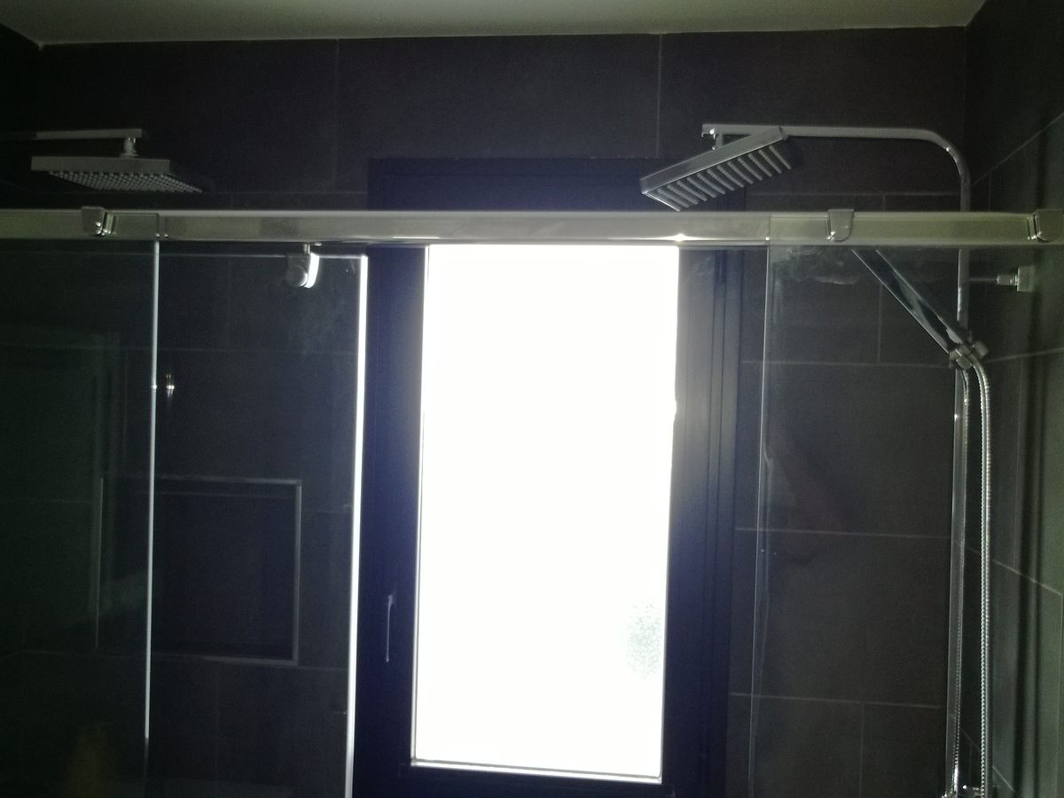 Baño del mismo ático terminado: ducha de obra de gran formato en tono oscuro con mampara de cristal