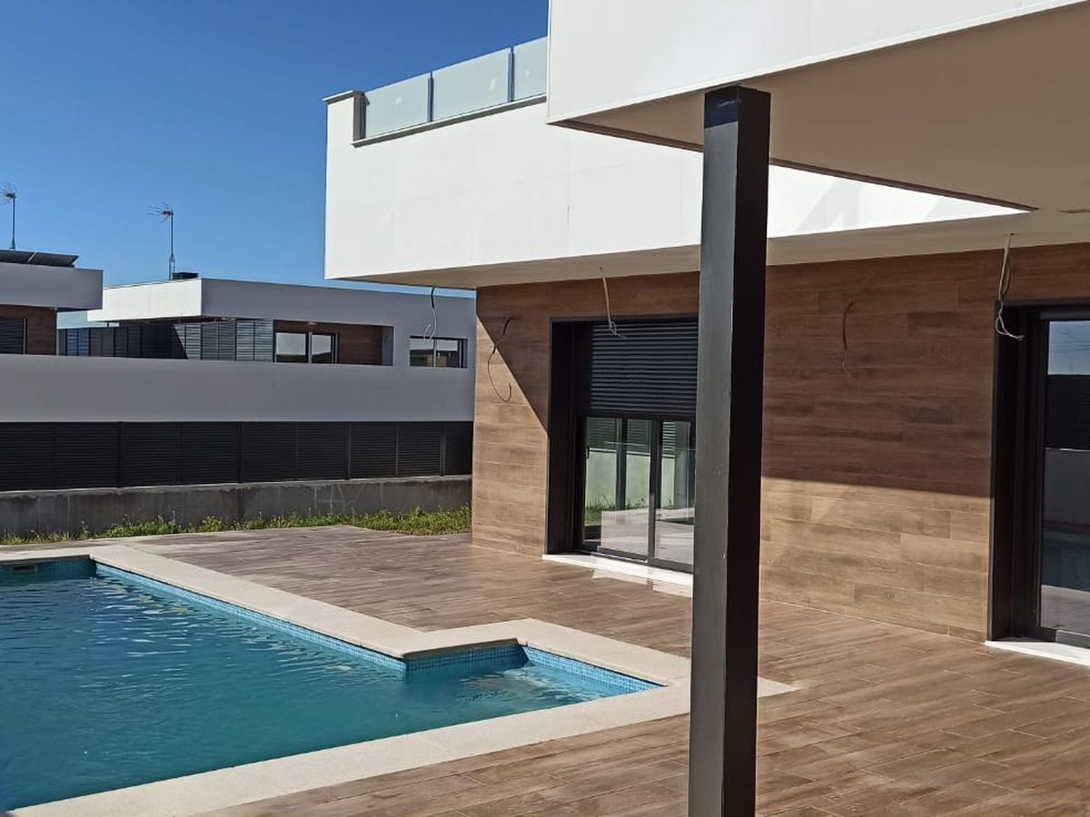 La misma piscina terminada y llena, con el solado colocado y la vivienda al fondo