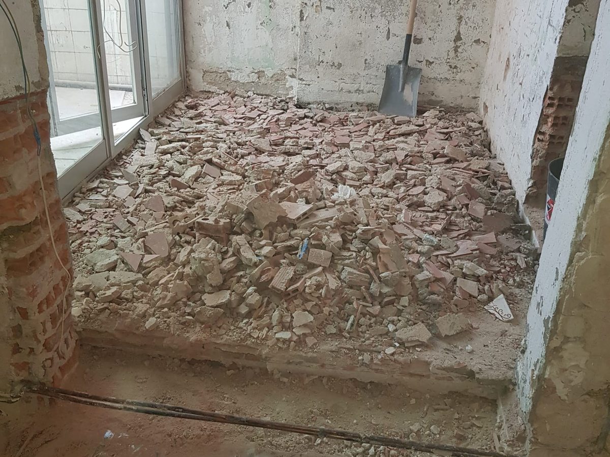 Vivienda antigua vaciada: suelo hidráulico original levantado y escombro por todo el estar