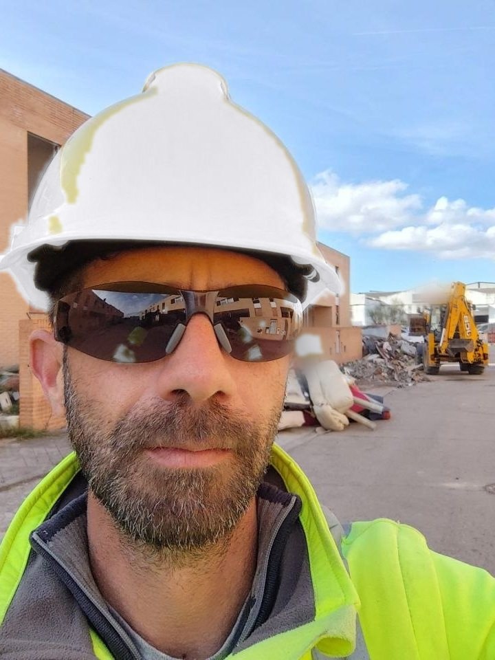 Jorge Navarro Navarro, Arquitecto Técnico, en obra con casco y chaleco reflectante, con la retroexcavadora y el acopio de escombro al fondo