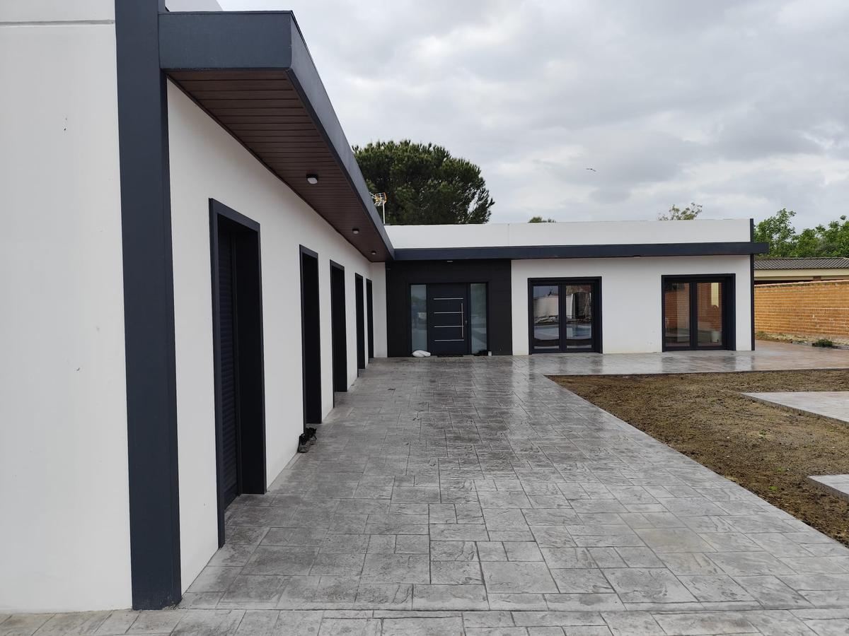 Fachada lateral con porche corrido y pavimento de hormigón impreso en una vivienda de una planta