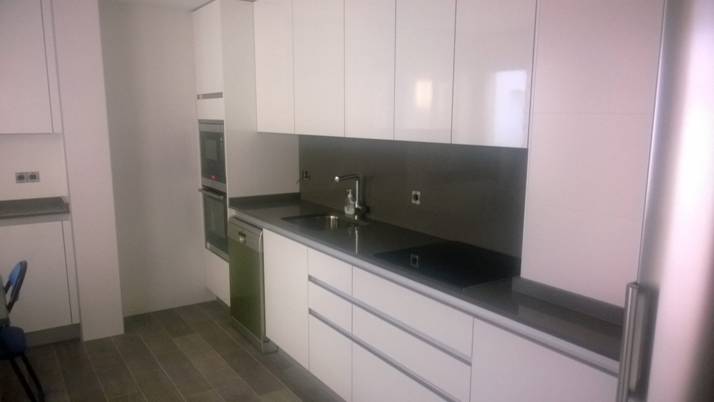 Cocina terminada con muebles blancos sin tirador, encimera oscura y columna de horno