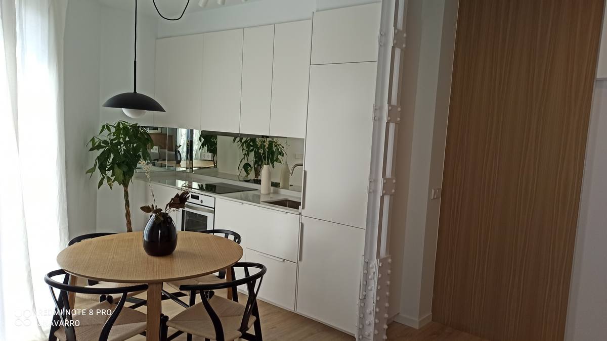 Cocina abierta terminada tras una reforma integral, con mesa redonda, frente de madera y luz natural