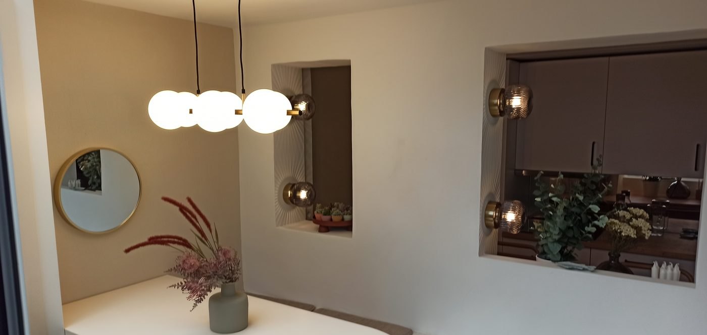 Comedor terminado tras la reforma, con lámpara de globos, hornacinas iluminadas y carpintería de madera